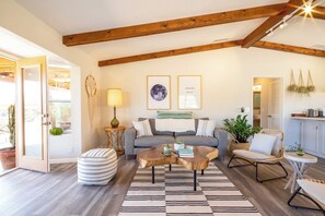 A living room with a sofa, coffee table, and chairs, wooden beams on the ceiling, and framed artwork on the wall.