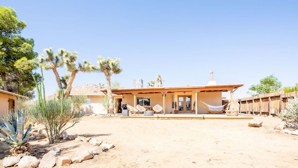A desert-style house with a covered patio, outdoor seating, and cacti.