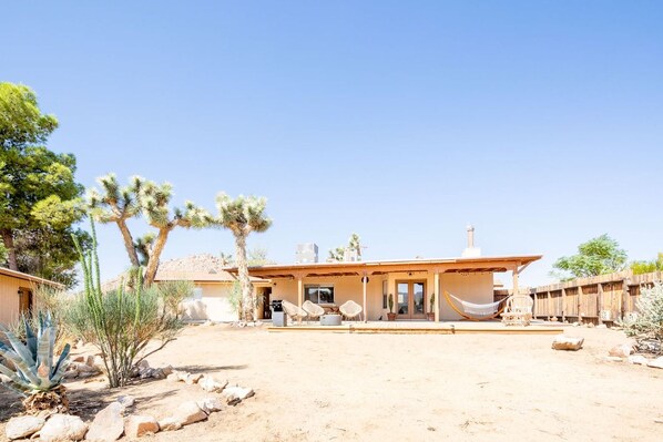 A desert-style house with a covered patio, outdoor seating, and cacti.