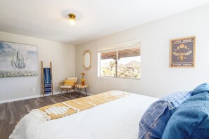A bedroom with a bed, a window, a chair, and a wall art piece.