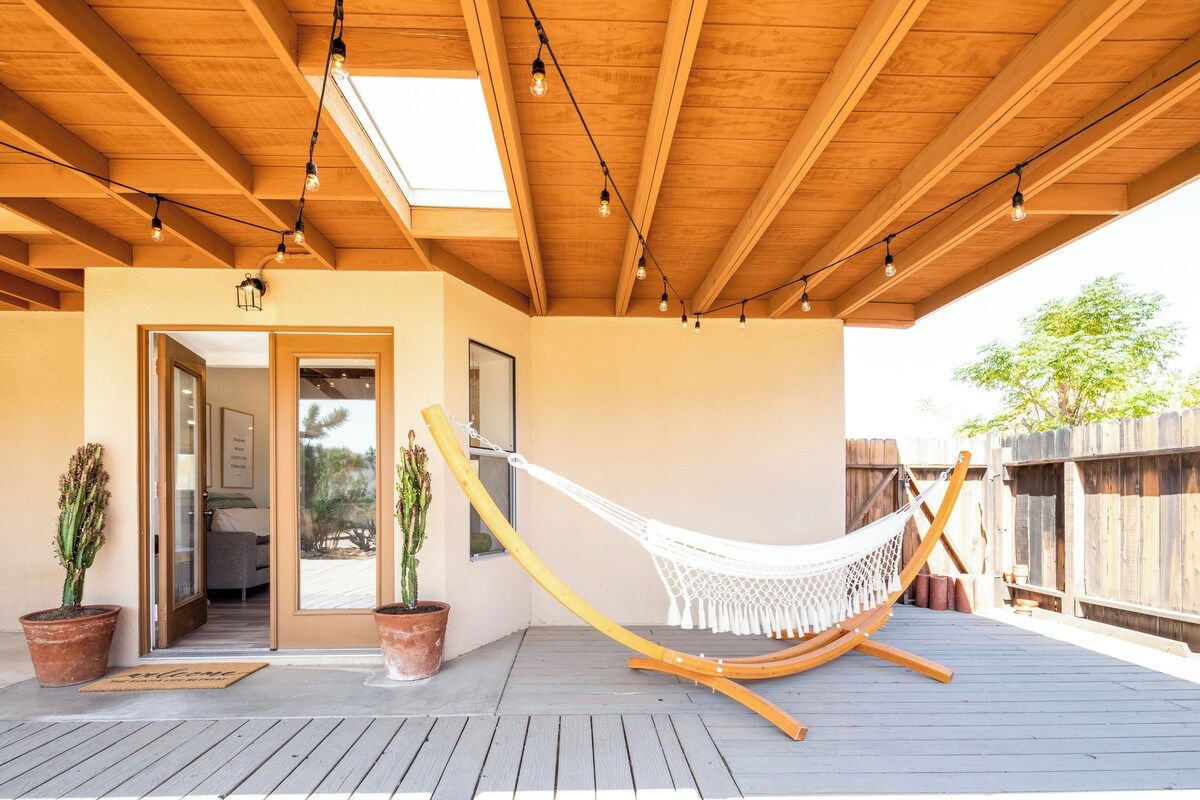 Une terrasse en bois avec un hamac, des plantes en pot et une porte donnant sur un espace intérieur.