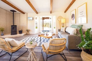 A cozy living room with a fireplace, wicker chairs, a sofa, and a view through an open door.