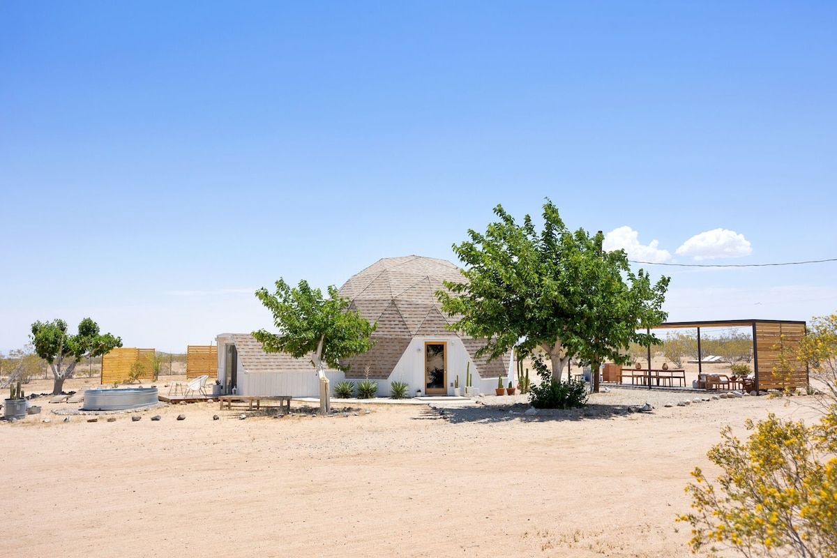A desert landscape with a single building featuring a dome-shaped roof and a small porch area.