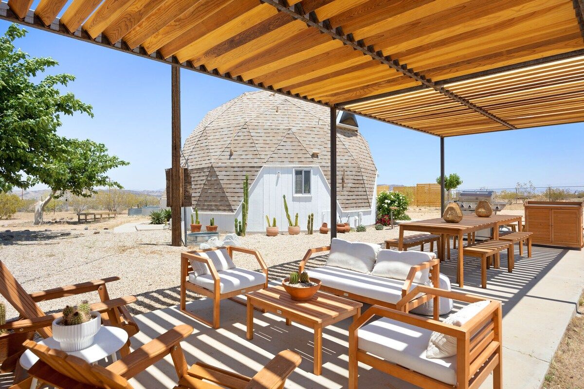 A covered outdoor seating area with wooden furniture and a dome-shaped structure in the background.