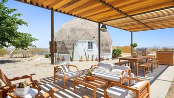 A covered outdoor seating area with wooden furniture and a dome-shaped structure in the background.