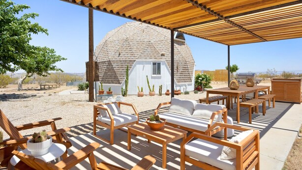 A covered outdoor seating area with wooden furniture and a view of a desert landscape.