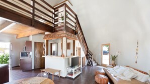 A spacious living area with a wooden staircase, a kitchen with modern appliances, and a cozy seating area with cushions.