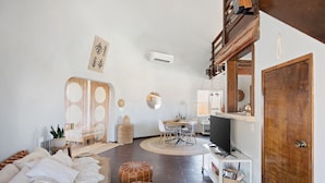 A modern living room with a sofa, ottomans, a dining table, and a TV.