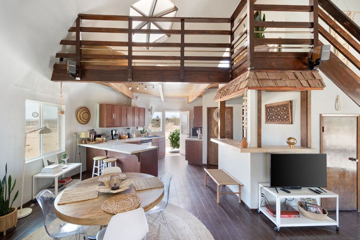 A spacious living area with a high ceiling, wooden beams, a central island, and a television on a stand.