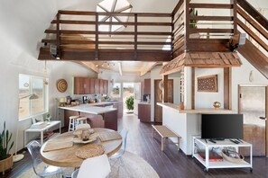 A spacious living area with a high ceiling, wooden beams, a central island, and a television on a stand.