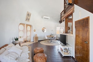 A modern living room with a sofa, ottomans, a dining area, and a television. - Abracadabra Dome in the Desert-Unique Experience! (Landers)