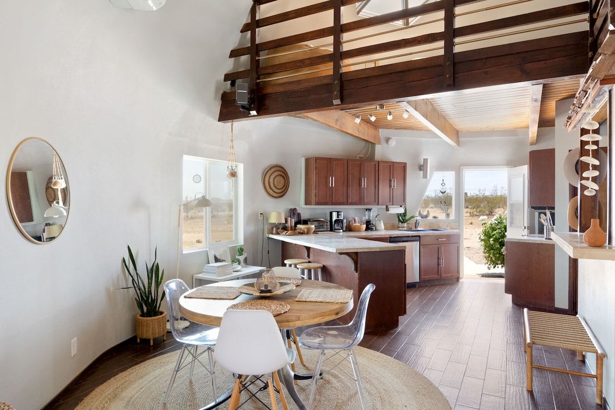 Une cuisine moderne dotée d’un îlot central, de poutres en bois au plafond et d’un coin repas avec une table ronde et des chaises.