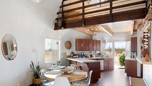 A modern kitchen with a central island, wooden ceiling beams, and a dining area with a round table and chairs. - Abracadabra Dome in the Desert-Unique Experience! (Landers)