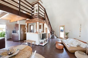 A spacious living area with a wooden staircase, a kitchen area, and a seating area with a sofa and ottomans.