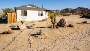 A single-story house with a white exterior, a wooden fence, and a desert landscape with cacti and rocks.