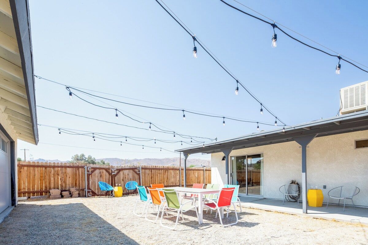Une terrasse extérieure avec une table et des chaises, des guirlandes lumineuses suspendues au-dessus et une clôture en bois en arrière-plan.