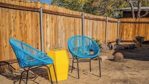 A fenced backyard with two blue chairs and a yellow stool.