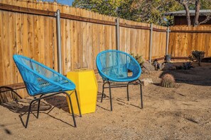 A fenced backyard with two blue chairs and a yellow stool.