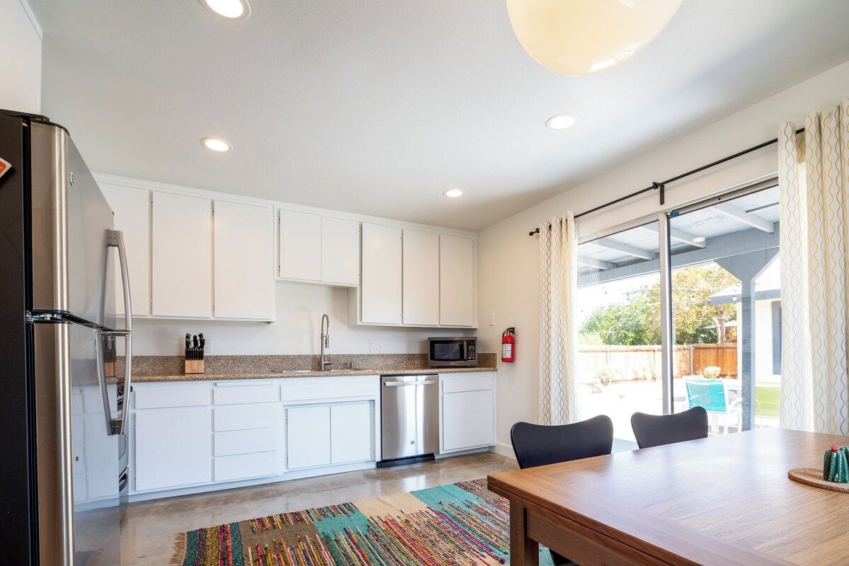 A modern kitchen with white cabinets, stainless steel appliances, and a dining area with a wooden table and chairs.