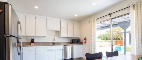 A modern kitchen with white cabinets, stainless steel appliances, and a dining area with a wooden table and chairs.