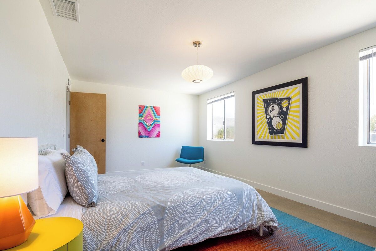A bedroom with a bed, a chair, a lamp, and artwork on the walls.
