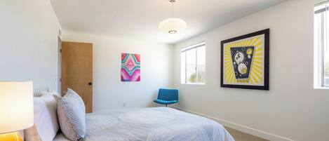 A bedroom with a bed, a chair, a lamp, and artwork on the walls.