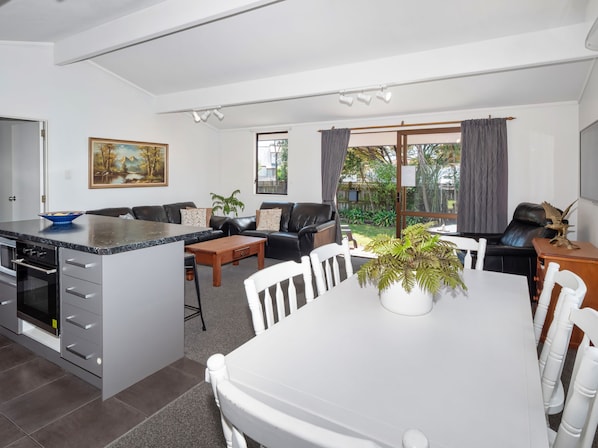 A modern kitchen with a marble countertop, a dining area with a white table and chairs, a black leather sofa, and a large window with curtains.