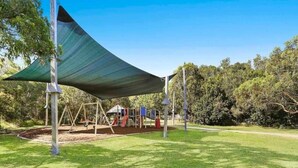 Un parque infantil con columpios y toboganes bajo una gran vela de sombra.
