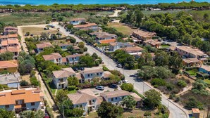 Vista aérea de una zona residencial costera con casas de tejados de terracota, un camino serpenteante y una playa al fondo.