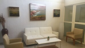 A living room with a white sofa, two armchairs, a coffee table, and two paintings on the wall.