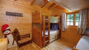 L'interno di una baita in legno con un letto a castello, una piccola panca e una finestra con tende.