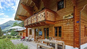 Un chalet in legno con un balcone, un'area pranzo con posti a sedere all'aperto e vista sulle montagne.