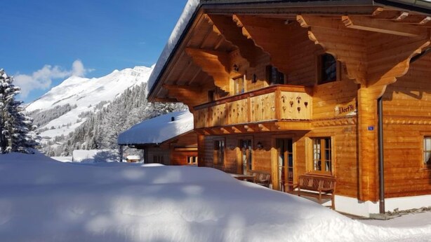 Un chalet in legno con un balcone, circondato da montagne innevate.