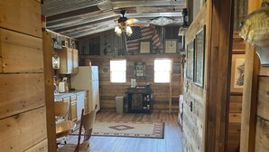 Ein rustikales Blockhaus-Interieur mit einer Essnische aus Holz, einer Küche und einer Leiter, die zu einem Schlafboden führt.