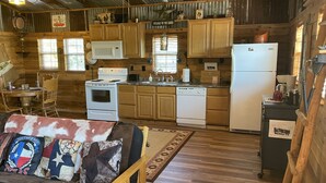 Ein rustikales Blockhaus-Interieur mit Holzwänden, einem Essbereich, einer Küche mit Holzausstattung, einem Kühlschrank und einer Couch mit Kissen im Texas-Stil.