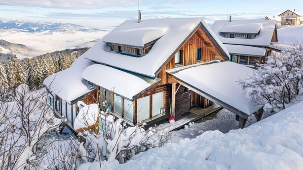 Ein modernes Chalet mit geneigtem Dach, großen Fenstern und Blick auf schneebedeckte Berge.