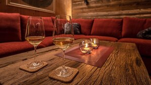 Ein Holztisch mit zwei Weingläsern und Untersetzern, ein rotes Sofa und ein gerahmtes Bild an der Wand.
