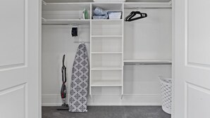 Un dressing où l’on peut entrer, équipé d’un aspirateur, d’une planche à repasser et de vêtements suspendus.