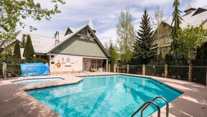 Une piscine avec, en arrière-plan, un bâtiment dont le toit est végétalisé, le tout entouré d’arbres et d’une clôture.