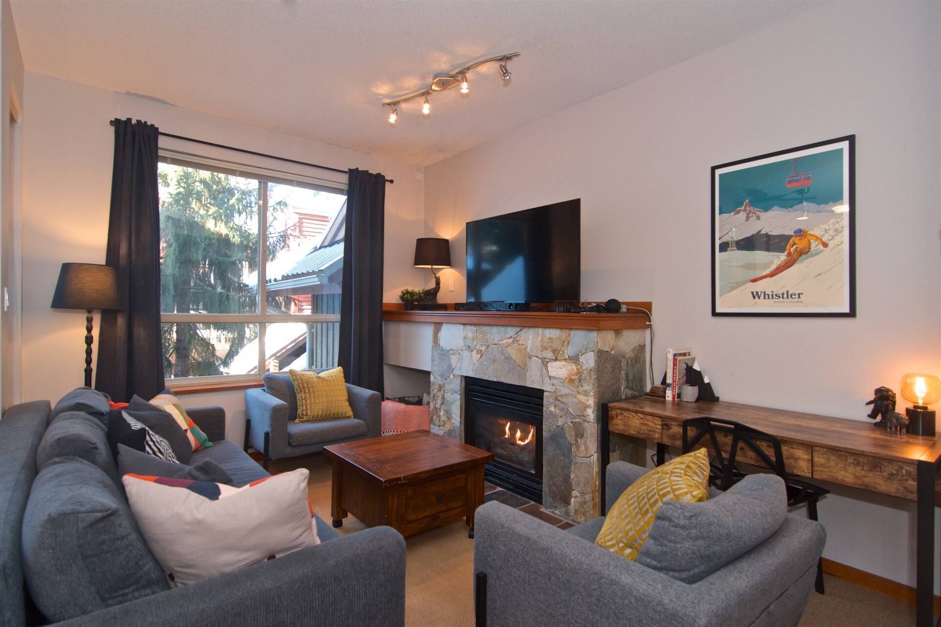 Un salon chaleureux avec une cheminée, des fauteuils confortables, un téléviseur à écran plat et une affiche représentant un paysage.