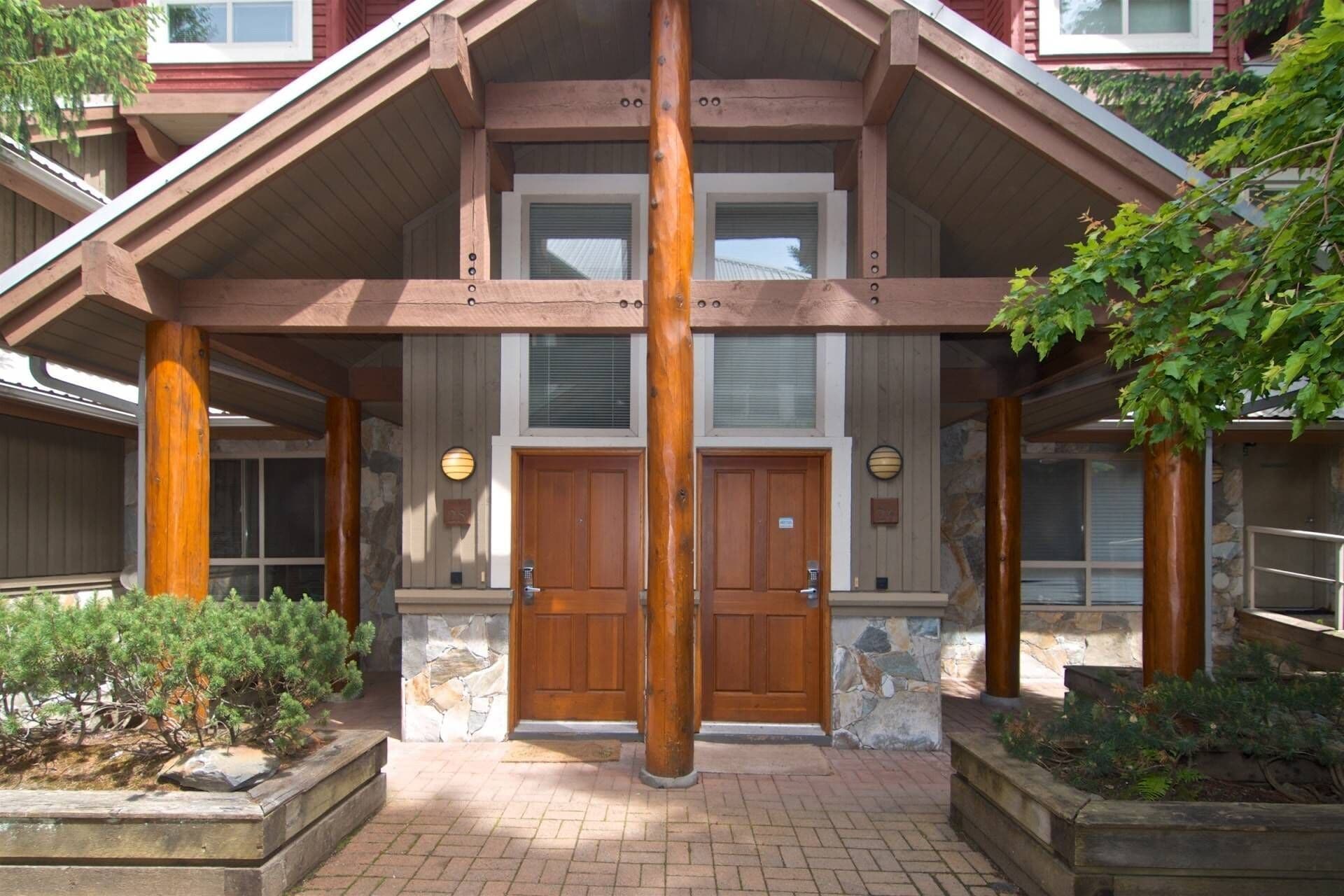 Un bâtiment à deux étages doté d’une façade symétrique, avec une entrée centrale encadrée de deux portes, flanquée de piliers en pierre et de poutres en bois.