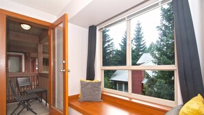 A room with a large window, a wooden bench, and a door leading to another space. - Quiet tranquil setting. Updated townhouse Free parking, walk to Village and shops, common hot tub, (Whistler)