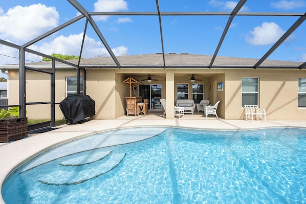 A swimming pool with a covered area, lounge chairs, and a pergola.