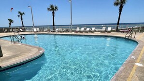 A clear blue pool with a deck area, surrounded by palm trees and lounge chairs.