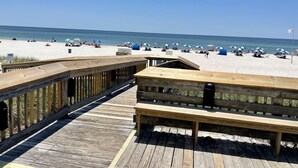 A wooden boardwalk leading to a beach with umbrellas and beach chairs.