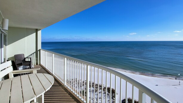 A balcony with a view of the ocean, a white railing, and a few chairs.