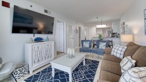A modern living room with a white entertainment unit, a large flat-screen TV, a brown sofa, and a blue patterned rug.