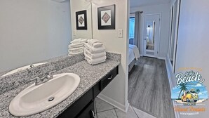 Une salle de bain avec un comptoir en granit, un lavabo et un miroir avec éclairage intégré. Des serviettes sont pliées et empilées sur le comptoir.