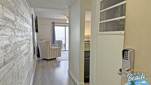 Un couloir avec un mur en bois, un coin salon avec un fauteuil et une porte dotée d’un système de verrouillage à clavier.