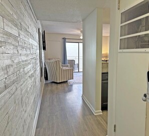 Un pasillo con pared de madera, una zona de estar con una silla y una puerta con cerradura electrónica.